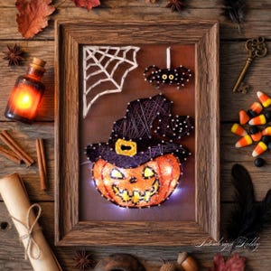 Peut inclure: Une œuvre d'art en ficelle d'Halloween encadrée représentant une citrouille orange portant un chapeau de sorcière noir. Une toile d'araignée blanche et une araignée noire sont également incluses dans la conception. L'œuvre est placée sur un fond marron et encadrée de bois rustique.