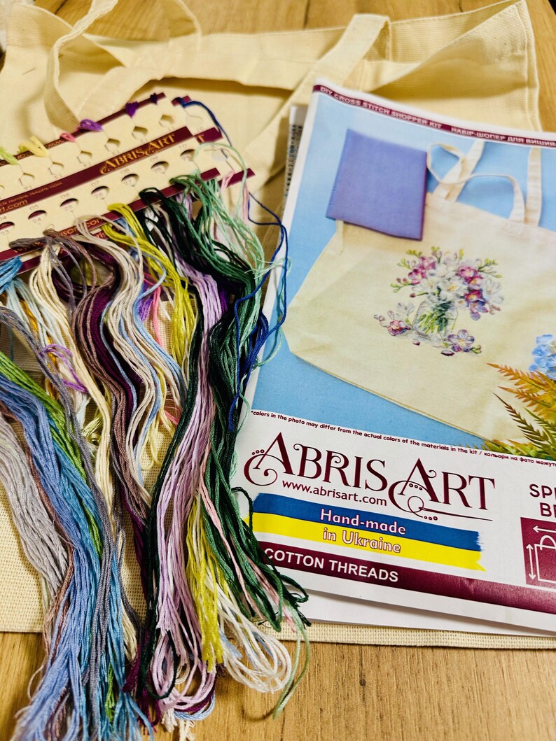 May include: A cross-stitch shopper kit with colorful cotton threads. The kit includes a tote bag, a pattern, and a variety of embroidery floss in shades of blue, green, purple, and yellow. The kit is hand-made in Ukraine.