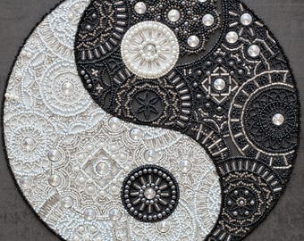 Op de afbeelding: Een zwart-wit yin yang symbool gemaakt van kralen. Het symbool is omgeven door een zwarte achtergrond.