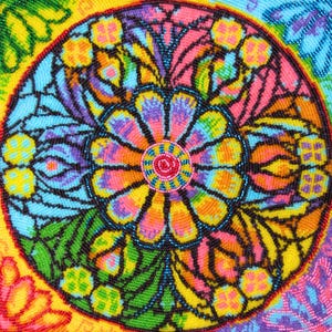 Könnte beinhalten: Ein kreisförmiges Textilstück mit einem lebendigen, mehrfarbigen Mandala-Muster. Das Design umfasst einen zentralen roten Kreis, umgeben von Schichten aus gelben, orangen, rosa, blauen und grünen Blumen- und geometrischen Formen mit schwarzer Umrandung.