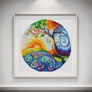 Può includere: Un ricamo a punto croce incorniciato che presenta un design circolare di un albero che attraversa le quattro stagioni. L'immagine mostra un sole, motivi vorticosi e colori vivaci che includono fili verdi, gialli, arancioni, viola e blu.