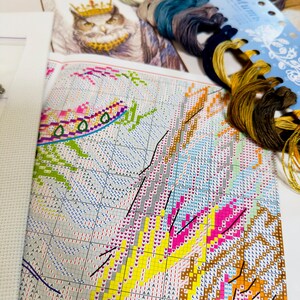 Puede incluir: Un kit de punto de cruz con un patr&oacute;n impreso, hilo de bordar y tela Aida. El patr&oacute;n presenta un dise&ntilde;o colorido con un b&uacute;ho con una corona. Los hilos son en tonos de azul, marr&oacute;n y dorado.