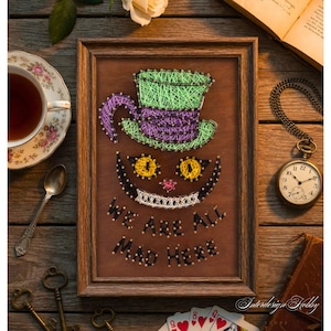 Puede incluir: Una pieza de arte de hilo enmarcada que representa al Gato de Cheshire de Alicia en el país de las maravillas. La sonrisa y el sombrero del gato están hechos con hilo verde, morado y amarillo sobre un fondo marrón. El texto "WE ARE ALL MAD HERE" está debajo.