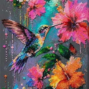 Op de afbeelding: Een gestructureerd kunstwerk van kralen op een donkergrijs canvas met een levendige kolibrie in vlucht, omringd door kleurrijke hibiscusbloemen in roze, oranje en witte tinten, met groene bladeren en verspreide kralenaccenten.