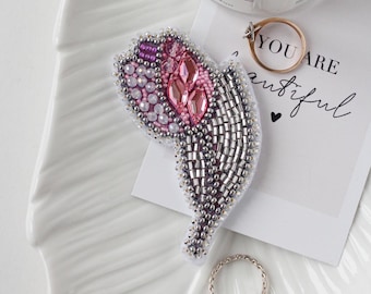 Può includere: Una spilla artigianale a forma di tulipano, caratterizzata da cristalli rosa sfaccettati, perline bianche iridescenti e perline metalliche argentate. Il design include una sezione superiore in perline rosa e uno stelo argentato perlato.