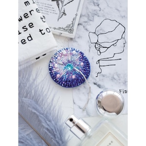 May include: A round, beaded, blue, pink and white ornament with a silver chain attached. The ornament has a sparkly, iridescent finish.