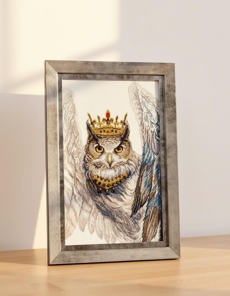 May include: Framed artwork featuring a detailed owl illustration. The owl is adorned with a golden crown and collar, set against a backdrop of detailed wings. The frame is a muted gray, adding a touch of elegance to the artwork.