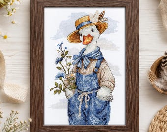 May include: A framed cross-stitch embroidery featuring a white goose wearing a yellow straw hat with a small flower, a blue neckerchief, and blue denim overalls. The goose holds a bouquet of blue and white wildflowers against a light blue sky.