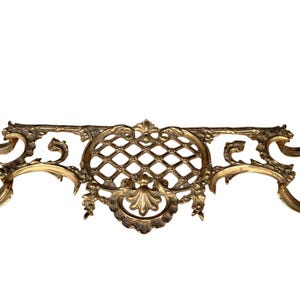 May include: Ornate, antique brass decorative element with a symmetrical design. Features a central diamond-patterned section, flanked by scrolling, floral accents. The brass has a warm, aged patina, suggesting vintage craftsmanship.