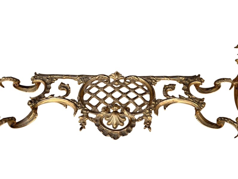 May include: Ornate, antique brass decorative element with a symmetrical design. Features a central diamond-patterned section, flanked by scrolling, floral accents. The brass has a warm, aged patina, suggesting vintage craftsmanship.