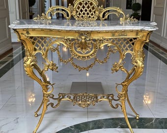 May include: An antique gold console table with a marble top. The table has elaborate scrollwork, a lattice back, and floral details. The legs are curved and end in ball feet. A luxurious piece of furniture, approximately 120 cm long.