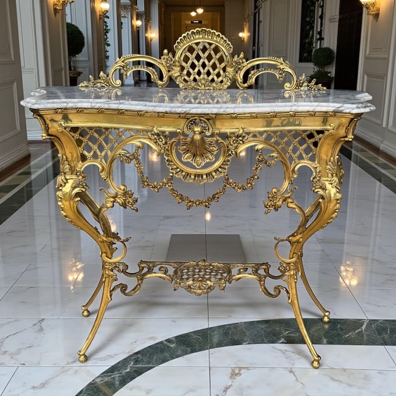 May include: Ornate gold console table with a marble top. The table features intricate scrollwork, a lattice back, and delicate floral details. The legs are curved and end in small ball feet. A luxurious piece of furniture.