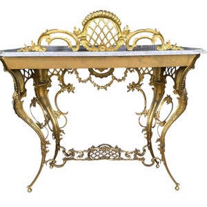 May include: An antique gold-colored console table with ornate detailing. The table features a marble top and intricate, curved legs. The design includes floral and scrollwork accents, with a decorative back panel. The table's height is approximately 30 inches.
