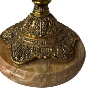 Pu&ograve; includere: Primo piano di una base di candelabro decorativa. La base &egrave; realizzata in pietra ovale marrone chiaro con una parte superiore in metallo dorato e ornato. La parte superiore in metallo presenta intricati disegni floreali e a volute.