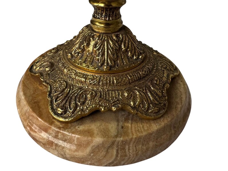 Pu&ograve; includere: Primo piano di una base di candelabro decorativa. La base &egrave; realizzata in pietra ovale marrone chiaro con una parte superiore in metallo dorato e ornato. La parte superiore in metallo presenta intricati disegni floreali e a volute.