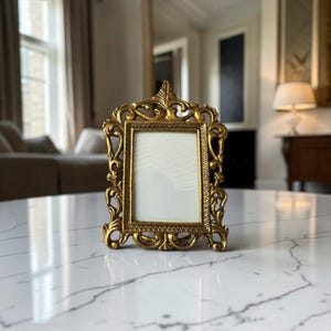 Op de afbeelding: Een rechthoekige fotolijst met een metallic gouden afwerking. De lijst is voorzien van ingewikkeld krulwerk en bladvormige details langs de buitenranden, rondom een effen wit middenstuk met een gestructureerd, lineair patroon.