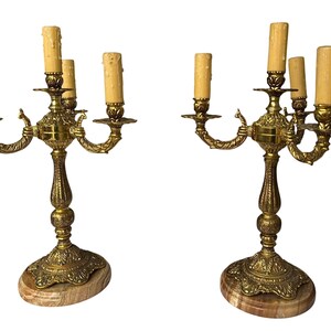 Pu&ograve; includere: Due candelabri antichi in ottone, ciascuno con cinque portacandele. Presentano dettagli intricati, basi in marmo e finte candele. L'ottone ha una calda patina invecchiata e il design &egrave; elegante e vintage.