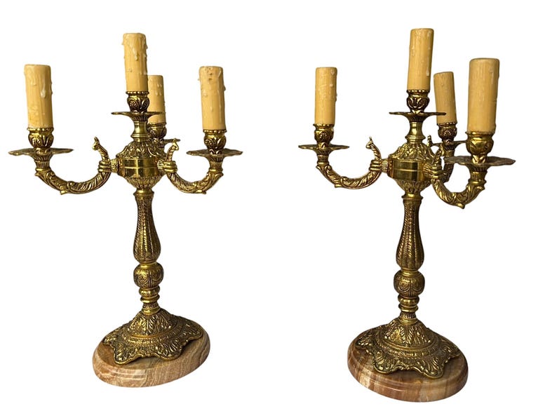 Pu&ograve; includere: Due candelabri antichi in ottone, ciascuno con cinque portacandele. Presentano dettagli intricati, basi in marmo e finte candele. L'ottone ha una calda patina invecchiata e il design &egrave; elegante e vintage.