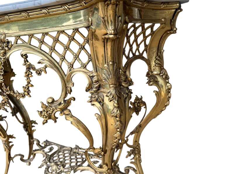 May include: Ornate gold-colored console table with a marble top. The table features intricate floral and lattice detailing, with curved legs and decorative accents. The design is reminiscent of antique furniture.