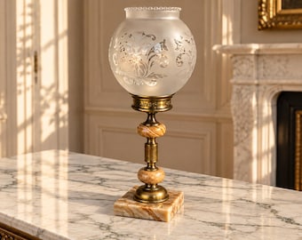 May include: A table lamp featuring a frosted glass globe shade with etched floral patterns, supported by a brass stem with two spherical marble accents, resting on a square marble base with a metallic finish on the hardware.