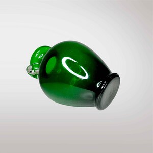 May include: A small, green glass vase with a rounded body and a clear glass handle.