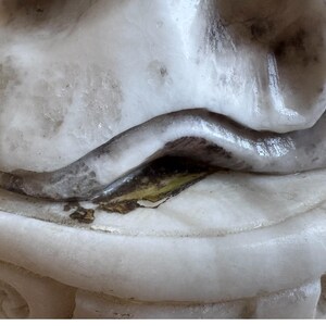 K&ouml;nnte beinhalten: Nahaufnahme eines wei&szlig;en Marmor-Skulpturenfragments. Die Skulptur hat eine geschwungene, glatte Form mit dunklem Akzent. Der Sockel ist rund mit geschnitzten Details.