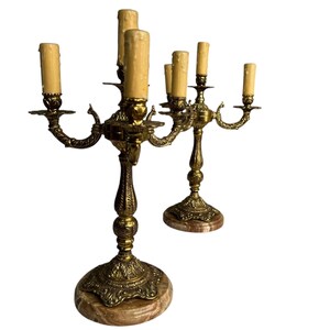 Pu&ograve; includere: Due candelabri antichi in ottone, ciascuno con cinque portacandele. I candelabri presentano dettagli ornati, basi in marmo e finte candele. I portacandele sono curvi verso l'esterno. Il design &egrave; vintage e decorativo.