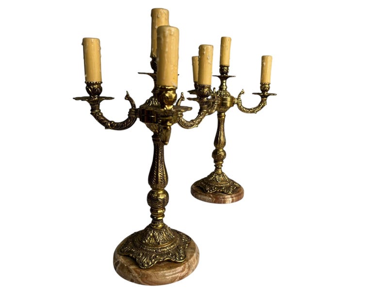 Pu&ograve; includere: Due candelabri antichi in ottone, ciascuno con cinque portacandele. I candelabri presentano dettagli ornati, basi in marmo e finte candele. I portacandele sono curvi verso l'esterno. Il design &egrave; vintage e decorativo.