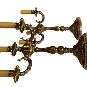 Pu&ograve; includere: Due candelabri antichi in ottone dorato. Ogni candelabro presenta tre bracci curvi per candele, con un motivo floreale dettagliato. Le basi sono rotonde con aspetto legno. Un accessorio decorativo per la casa.