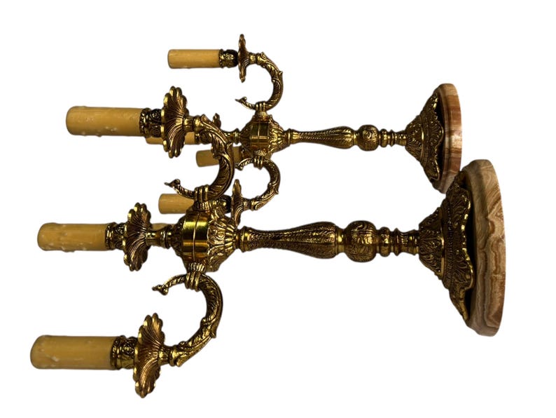 Pu&ograve; includere: Due candelabri antichi in ottone dorato. Ogni candelabro presenta tre bracci curvi per candele, con un motivo floreale dettagliato. Le basi sono rotonde con aspetto legno. Un accessorio decorativo per la casa.
