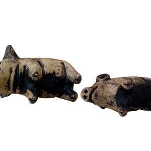 Pu&ograve; includere: Due statuette di maiale in ceramica, una in piedi e una sulla schiena. I maiali sono beige con dettagli neri, che mostrano caratteristiche dettagliate. Queste statuette decorative aggiungono un tocco rustico a qualsiasi arredamento.