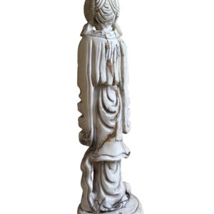 K&ouml;nnte beinhalten: Eine cremefarbene Vintage-Figur einer Frau in einem flie&szlig;enden Kleid, von hinten gesehen. Die Statue weist aufwendige Details in Haar und Kleidung auf, mit einem runden Sockel. Die Figur weist Altersspuren mit braunen Verf&auml;rbungen auf.