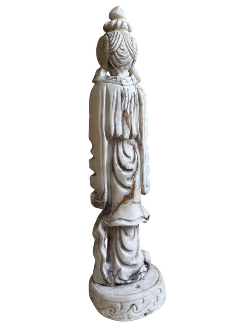 K&ouml;nnte beinhalten: Eine cremefarbene Vintage-Figur einer Frau in einem flie&szlig;enden Kleid, von hinten gesehen. Die Statue weist aufwendige Details in Haar und Kleidung auf, mit einem runden Sockel. Die Figur weist Altersspuren mit braunen Verf&auml;rbungen auf.