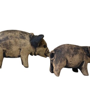 Pu&ograve; includere: Due statuette di maiali in ceramica. I maiali sono color beige con accenti neri sulle orecchie e sui musi. Le statuette hanno dettagli strutturati e sono posizionate come se interagissero tra loro. Lo sfondo &egrave; bianco.