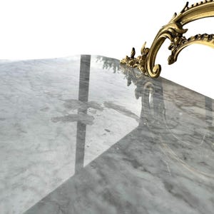 May include: Close-up of a marble surface with gray and white veining. A decorative gold-colored metal accent with ornate scrollwork is visible in the upper right corner. The surface reflects light.