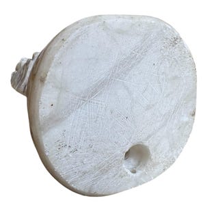 K&ouml;nnte beinhalten: Eine ovale Marmorskulptur in Wei&szlig; mit einem geschnitzten Blumendesign auf einer Seite. Die Unterseite hat ein kreisf&ouml;rmiges Loch. Die Oberfl&auml;che weist Kratzer und Unvollkommenheiten auf, was ihr ein rustikales Aussehen verleiht.