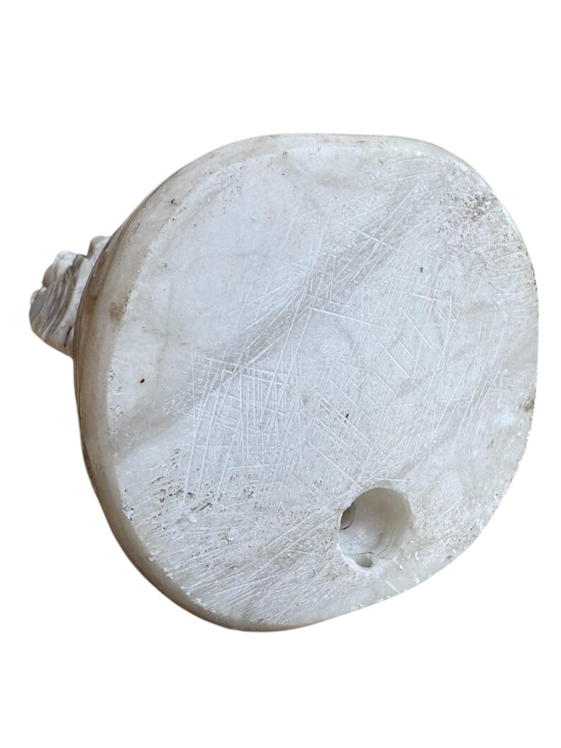 K&ouml;nnte beinhalten: Eine ovale Marmorskulptur in Wei&szlig; mit einem geschnitzten Blumendesign auf einer Seite. Die Unterseite hat ein kreisf&ouml;rmiges Loch. Die Oberfl&auml;che weist Kratzer und Unvollkommenheiten auf, was ihr ein rustikales Aussehen verleiht.