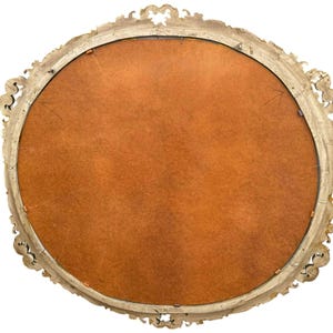 May include: An antique, oval-shaped mirror with a gold-colored, ornate frame. The back of the mirror is visible, featuring a warm, brown backing. The frame has detailed scrollwork and decorative elements.