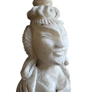 K&ouml;nnte beinhalten: Eine geschnitzte Statue aus wei&szlig;em Marmor einer ruhigen Figur mit aufwendigem Kopfschmuck und flie&szlig;enden Gew&auml;ndern. Die Statue hat ein sanftes L&auml;cheln und detaillierte Gesichtsz&uuml;ge, die die Handwerkskunst der Skulptur zeigen.