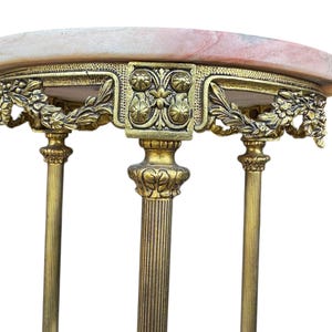 May include: An antique side table with a pink and white marble top. The table has ornate gold-coloured metalwork with floral and leaf designs. The table has three decorative legs.
