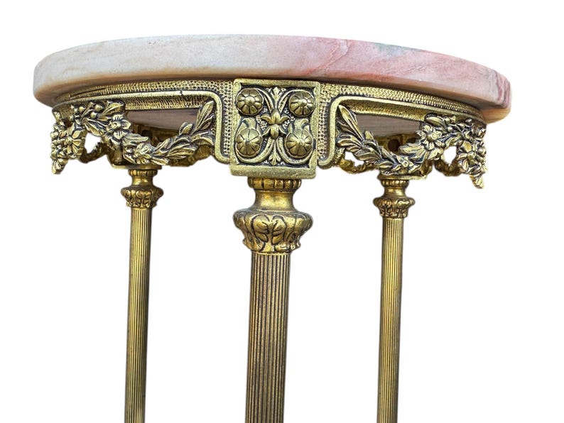 May include: An antique side table with a pink and white marble top. The table has ornate gold-coloured metalwork with floral and leaf designs. The table has three decorative legs.