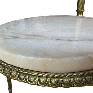 May include: A small, antique side table with a round, cream marble top. The table has ornate, gold-coloured metal legs and a decorative edge. The marble top has subtle brown veining. The table is likely used for decorative purposes.