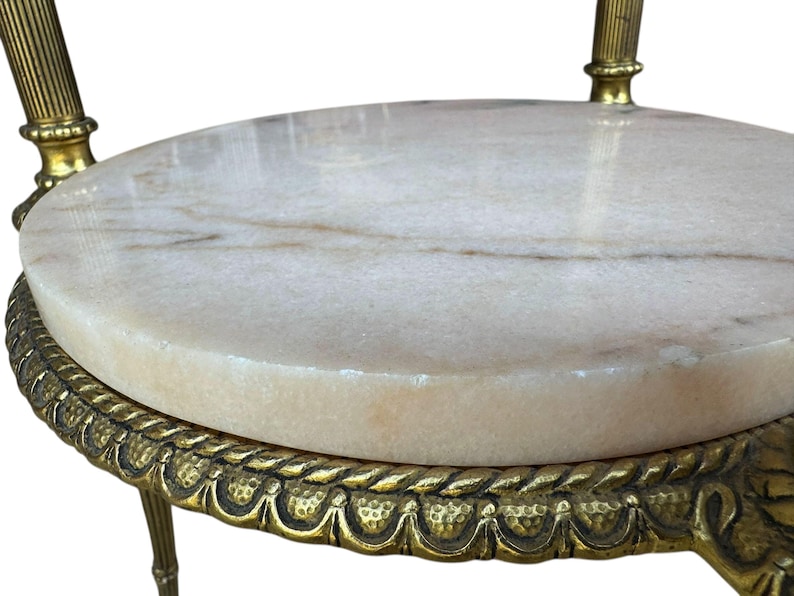 May include: A small, antique side table with a round, cream marble top. The table has ornate, gold-coloured metal legs and a decorative edge. The marble top has subtle brown veining. The table is likely used for decorative purposes.