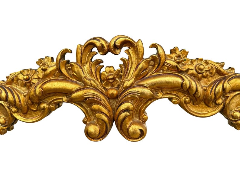 May include: Ornate gold-colored decorative architectural element with a symmetrical design. The element features floral and scroll motifs, with a detailed, textured surface. The piece is likely part of a larger decorative frame or molding.