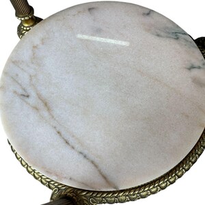 May include: A circular marble table top with a brass-coloured metal frame. The marble is white with grey and brown veining. The frame has a decorative rope-like edge and ornate legs.