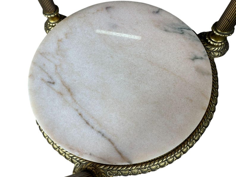 May include: A circular marble table top with a brass-coloured metal frame. The marble is white with grey and brown veining. The frame has a decorative rope-like edge and ornate legs.