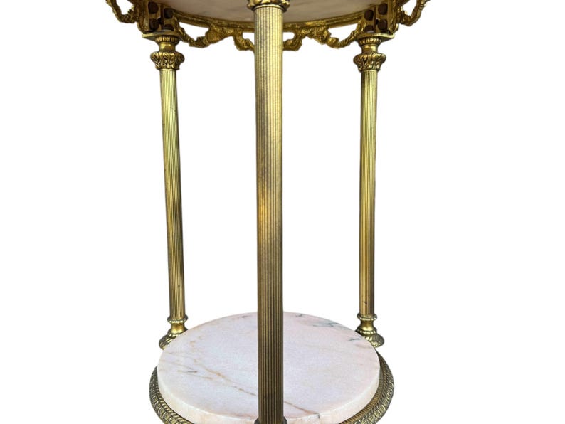 May include: An ornate side table in gold tones, featuring a marble top and base. The table has three fluted legs and decorative trim. The marble displays light pink and white veining. The table's height is approximately 76 cm.