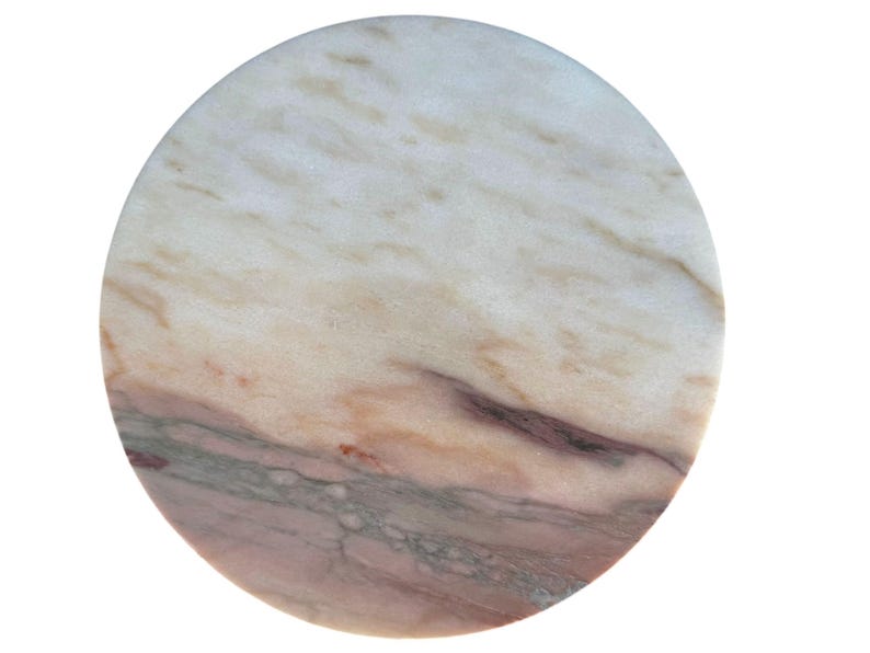 May include: A circular marble coaster with a natural, veined pattern. The coaster displays a mix of white, beige, pink, and grey tones, creating a unique design. Suitable for protecting surfaces from drink condensation.