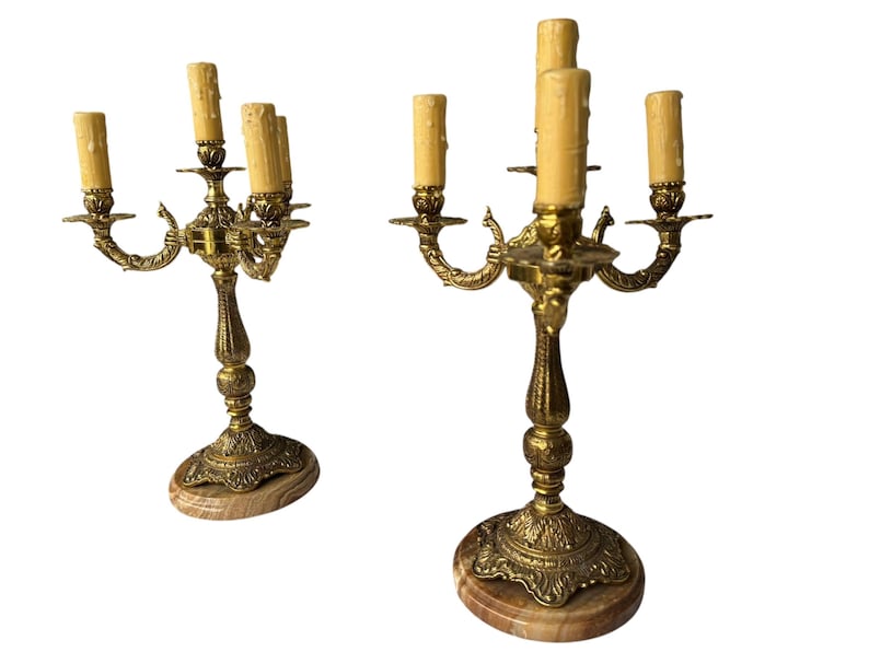 Pu&ograve; includere: Due candelabri antichi in ottone, ciascuno con cinque portacandele. I candelabri presentano dettagli ornati e poggiano su basi di marmo. Le candele sono di colore beige chiaro.
