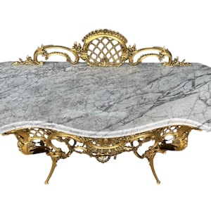 May include: An ornate, antique table with a gray marble top and gold-colored, filigree metalwork base. The table has a unique, curved shape and decorative detailing, showcasing a classic, elegant design.